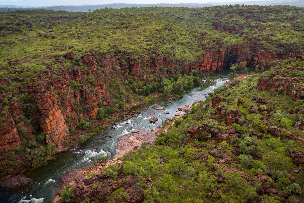A cragged, tree-lined gorge on Bullo River Station property in the Top End with a rushing river between the cliff face