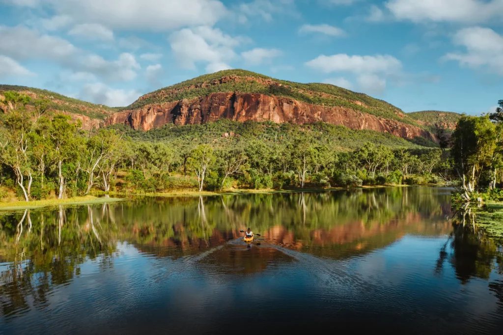 Guest kayaking along the weir alongside Mount Mulligan Lodge in Queensland with towering escarpment in the background