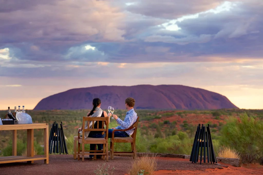 Couple toasting glasses at an outdoor dinner setting overlooking Uluru in the Northern Territory.  