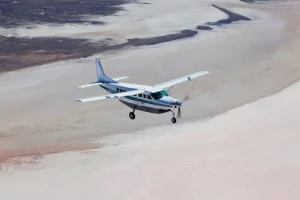 A Cessna Caravan aircraft with propeller in motion flying across a salt lake.