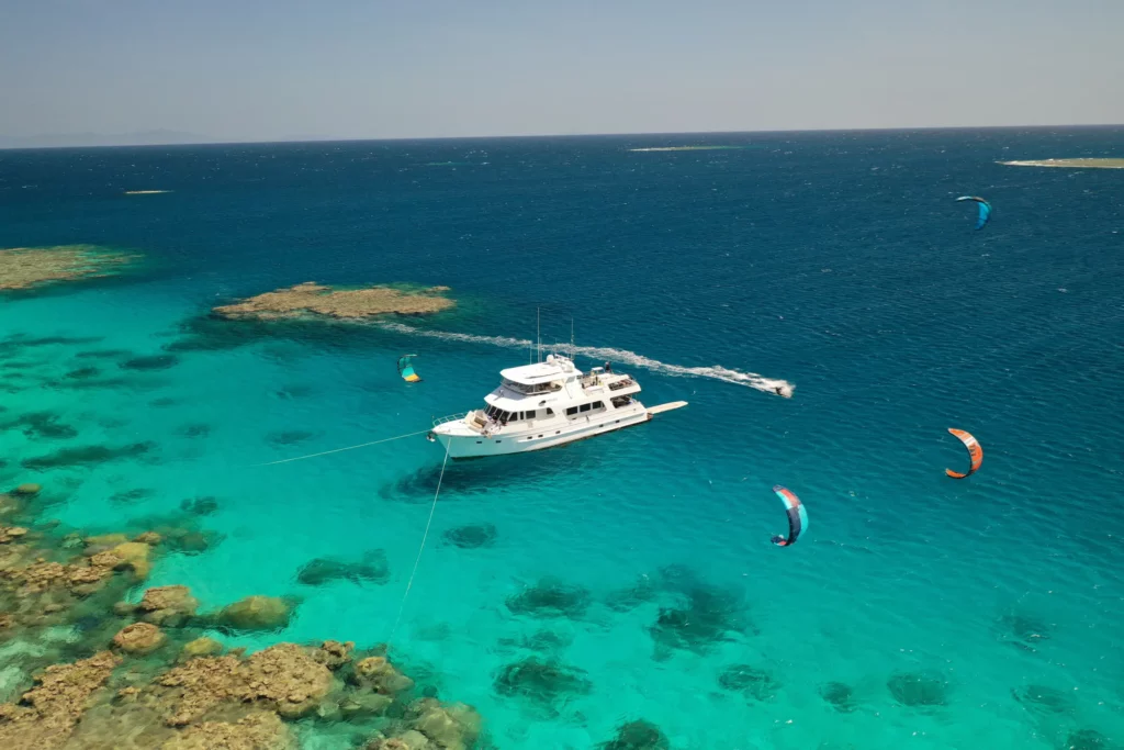 Aroona Luxury Boat Charters anchored on the Great Barrier Reef alongside corals with guests paragliding