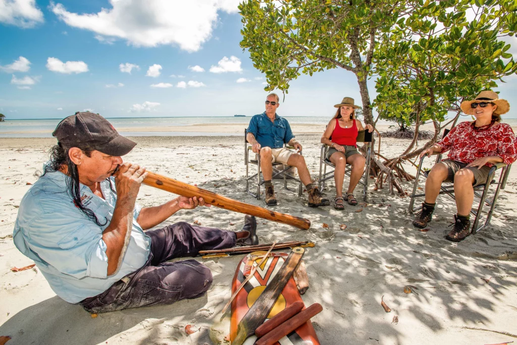 Kuku Yalanji Aboriginal Elder Mooks playing didgeridoo on a beach