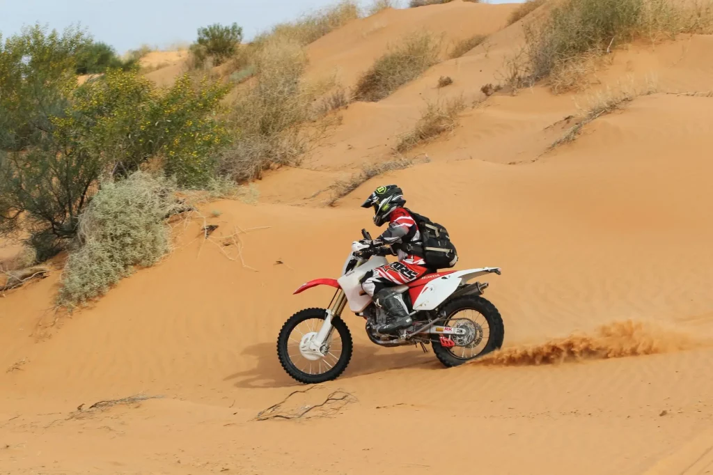 Motorbike rider in motion through the warm ochre of the Simpson Desert on the Madigan Line tour