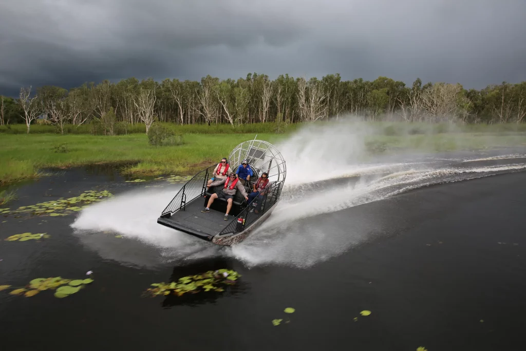 Four guests on an airboat in rapid motion through Australia’s Top End floodplains lined with greenery