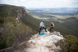 Two people set up to abseil over a cliff over a valley in the Blue Mountains, New South Wales