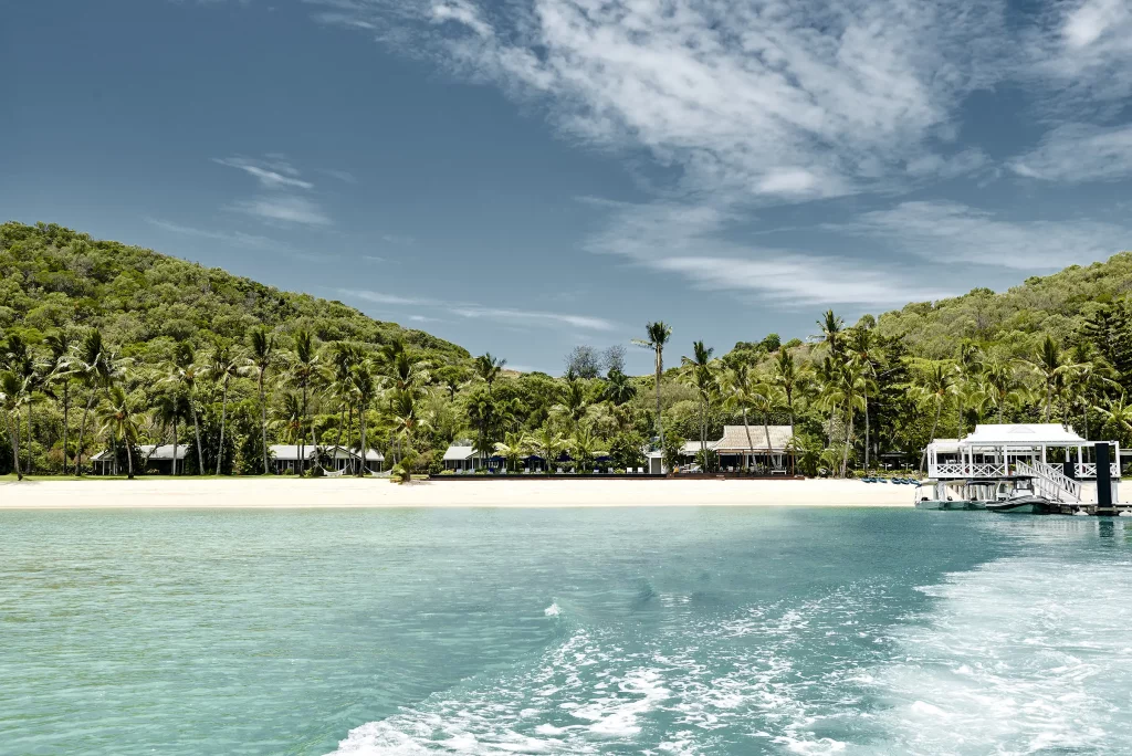 Views of Orpheus Island Lodge from the water, flanked by tropical green palms and white sand