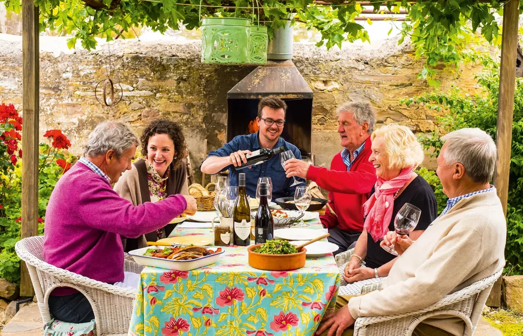 Six people happily sharing food and wine around a table in the Hutton Vale courtyard