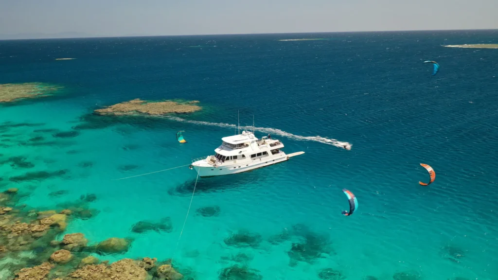 Aroona Luxury Boat Charters anchored on the Great Barrier Reef alongside corals with guests paragliding