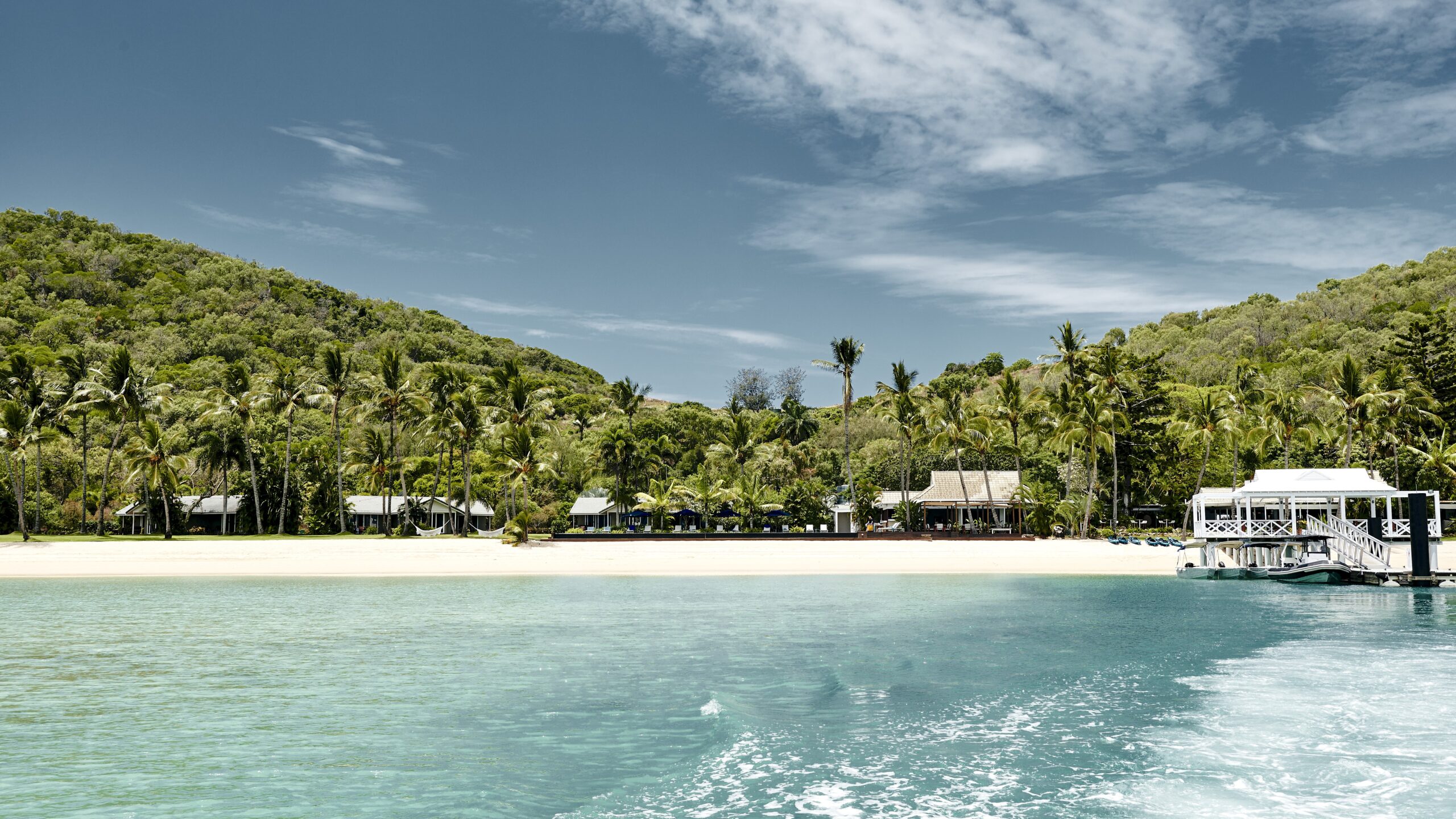 Views of Orpheus Island Lodge from the water, flanked by tropical green palms and white sand
