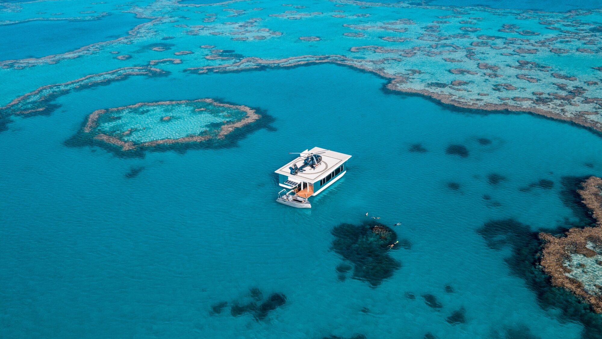 An areal ocean view of a reef and a boat with a helicopter on it.