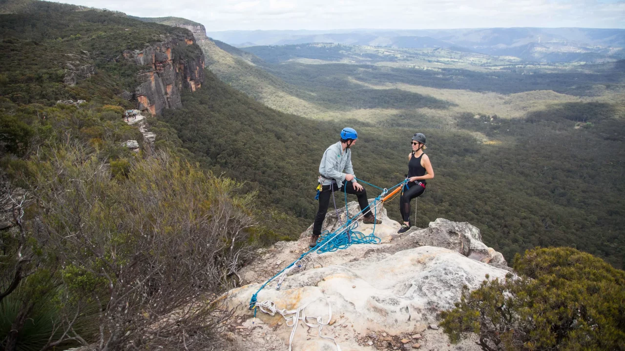 Two people set up to abseil over a cliff over a valley in the Blue Mountains, New South Wales